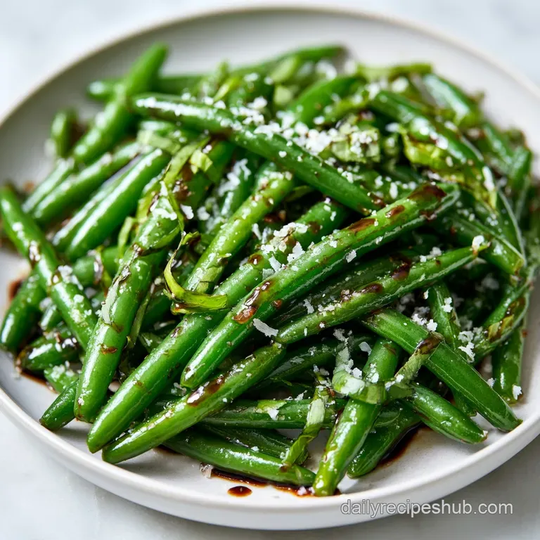 Bright green blanched beans drizzled with dark balsamic glaze and scattered basil leaves on a minimalist ceramic plate.