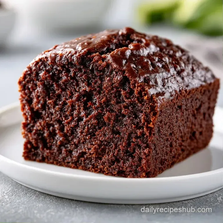 A thick slice of dark cocoa cake on a white ceramic plate, garnished with fresh raspberries and mint leaves.
